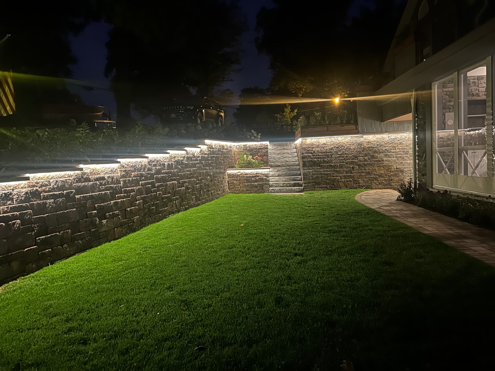 LED-lit stone retaining wall illuminating a vivid green lawn at night